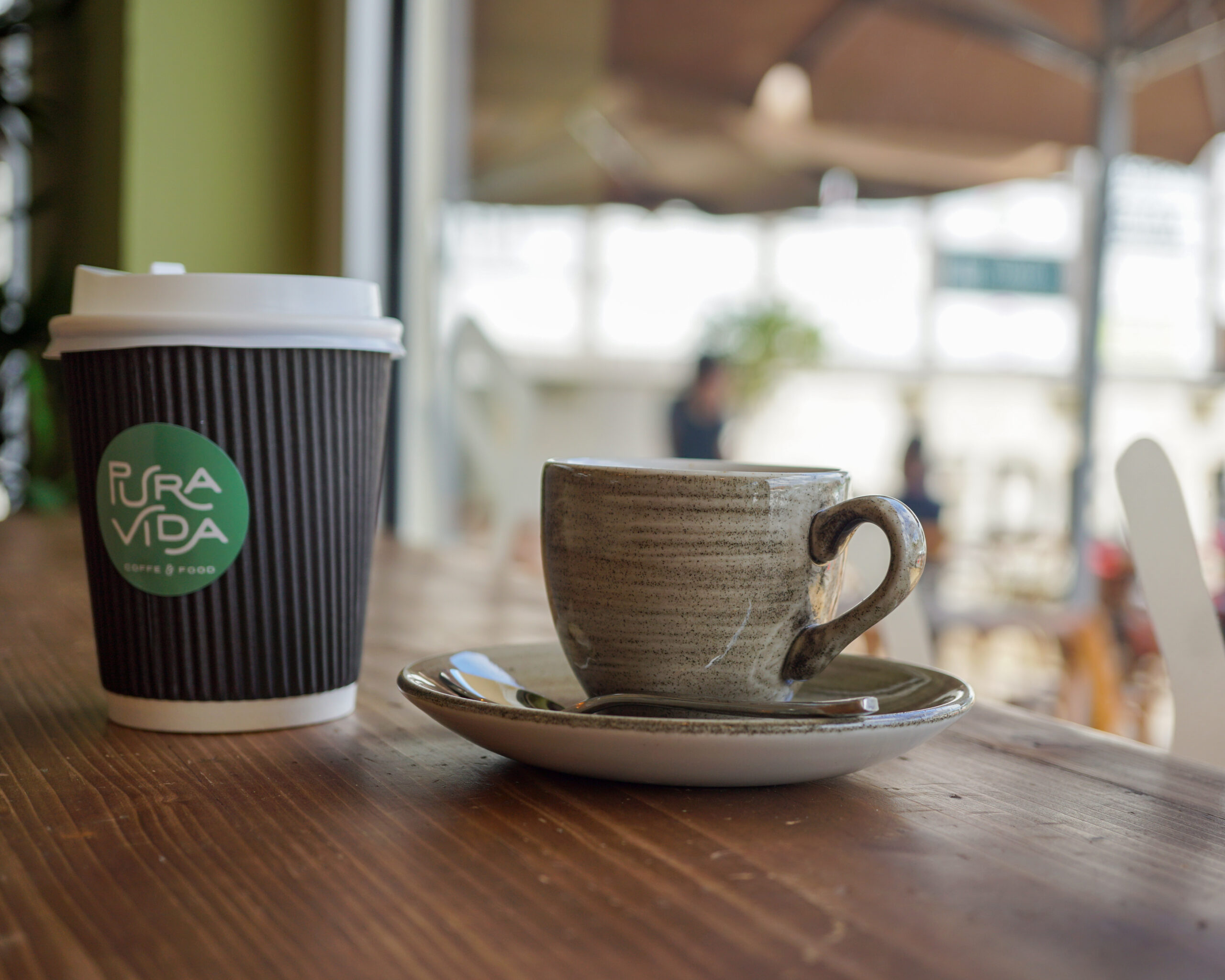 Cup of coffee beside green leaves on a calm green surface